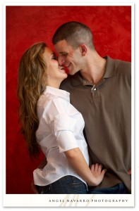 Engaged couple posing before a vibrant red wall.
