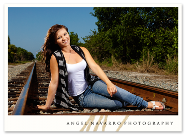 Girl seated on railroad tracks for her senior portrait.