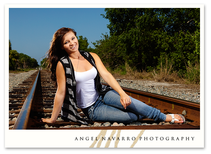 Girl seated on railroad tracks for her senior portrait.